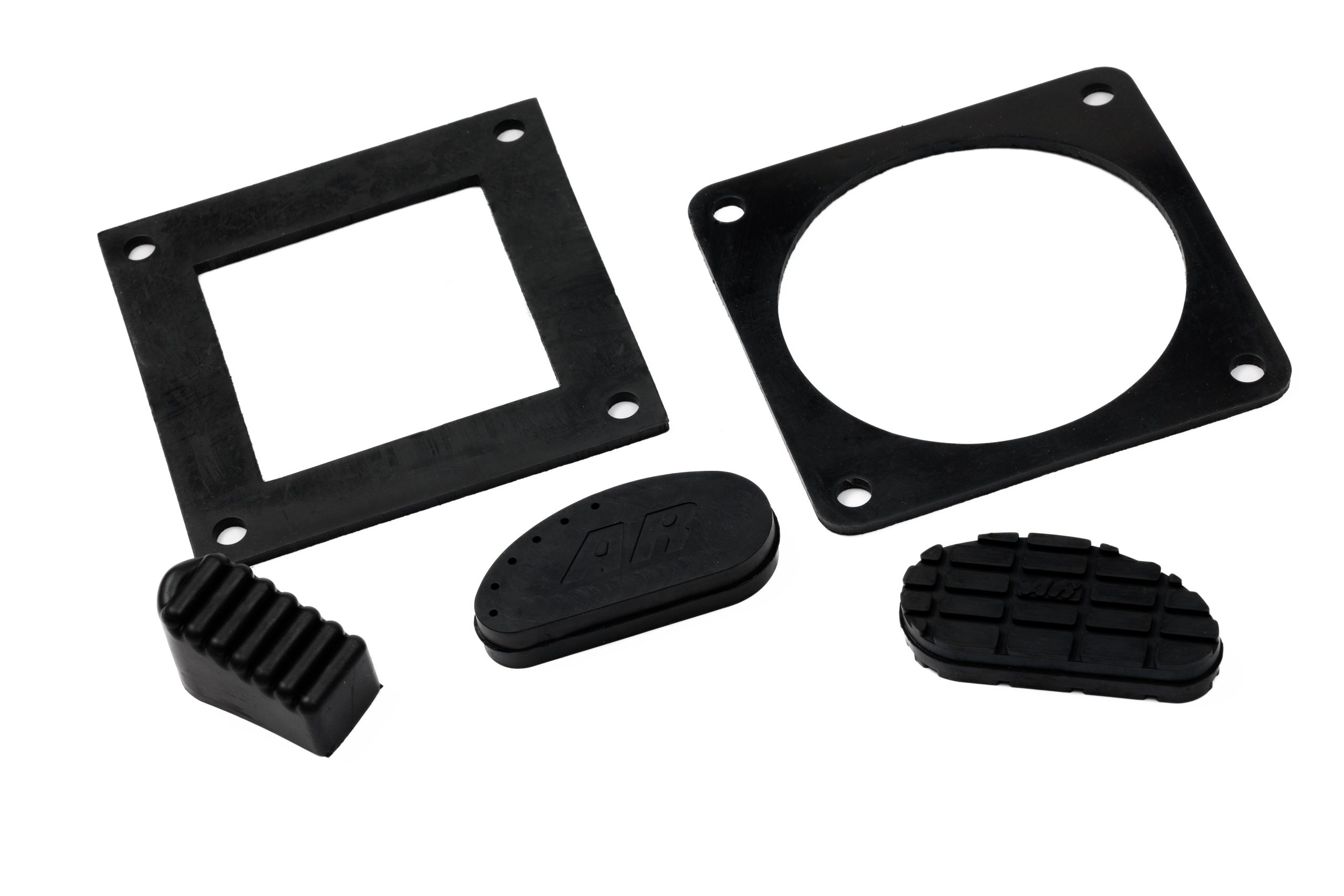 Two square black rubber gaskets, one with a square cutout and one with a circular cutout, shown from an angled top-down perspective alongside a ribbed rubber wedge and two textured oval pads on a white background.